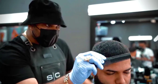 A barber working with a comb on the top of the hair.