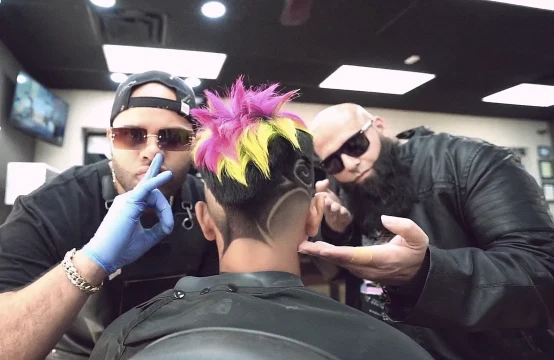 Two barbers working on a colorful hairstyle with a side design.