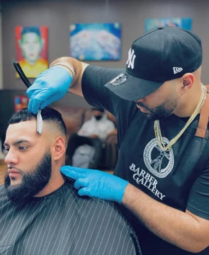 Tulpi, wearing blue gloves, details rapper ESKOMILI’s haircut with a razor at Barber Gallery.