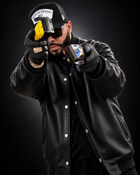 Tulpi wearing a black jacket, cap and gloves, holding two barber clippers against a dark background.